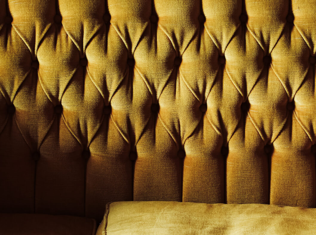 Close-up of tufted avocado-green velvet seating at The Code Austin with soft, moody lighting.