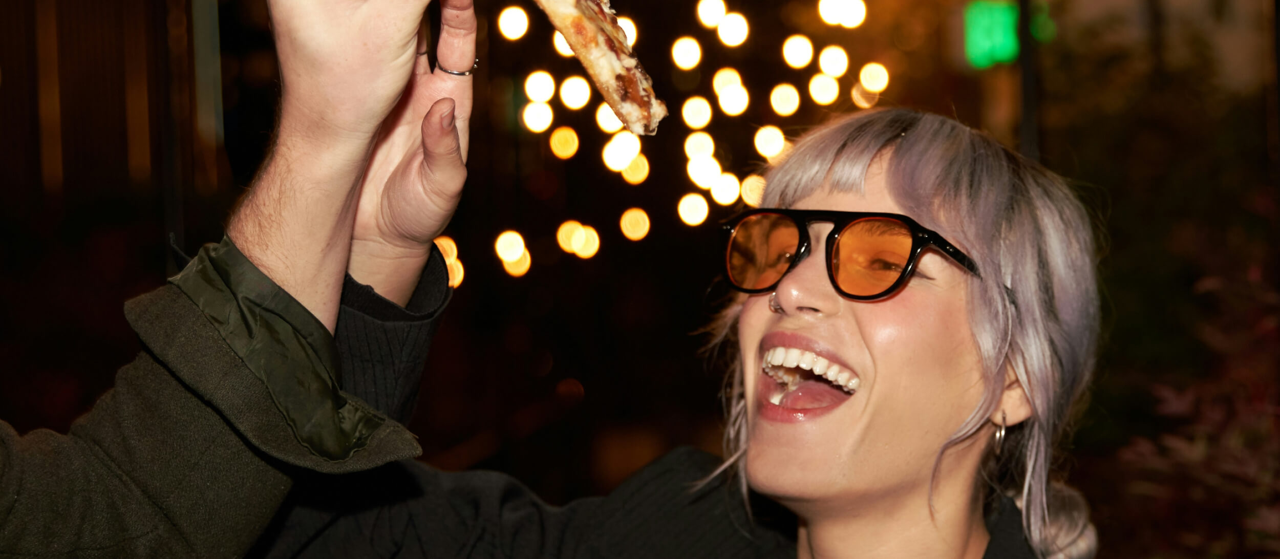 Young woman laughing at a nighttime gathering at The Code Austin with string lights glowing in the courtyard.